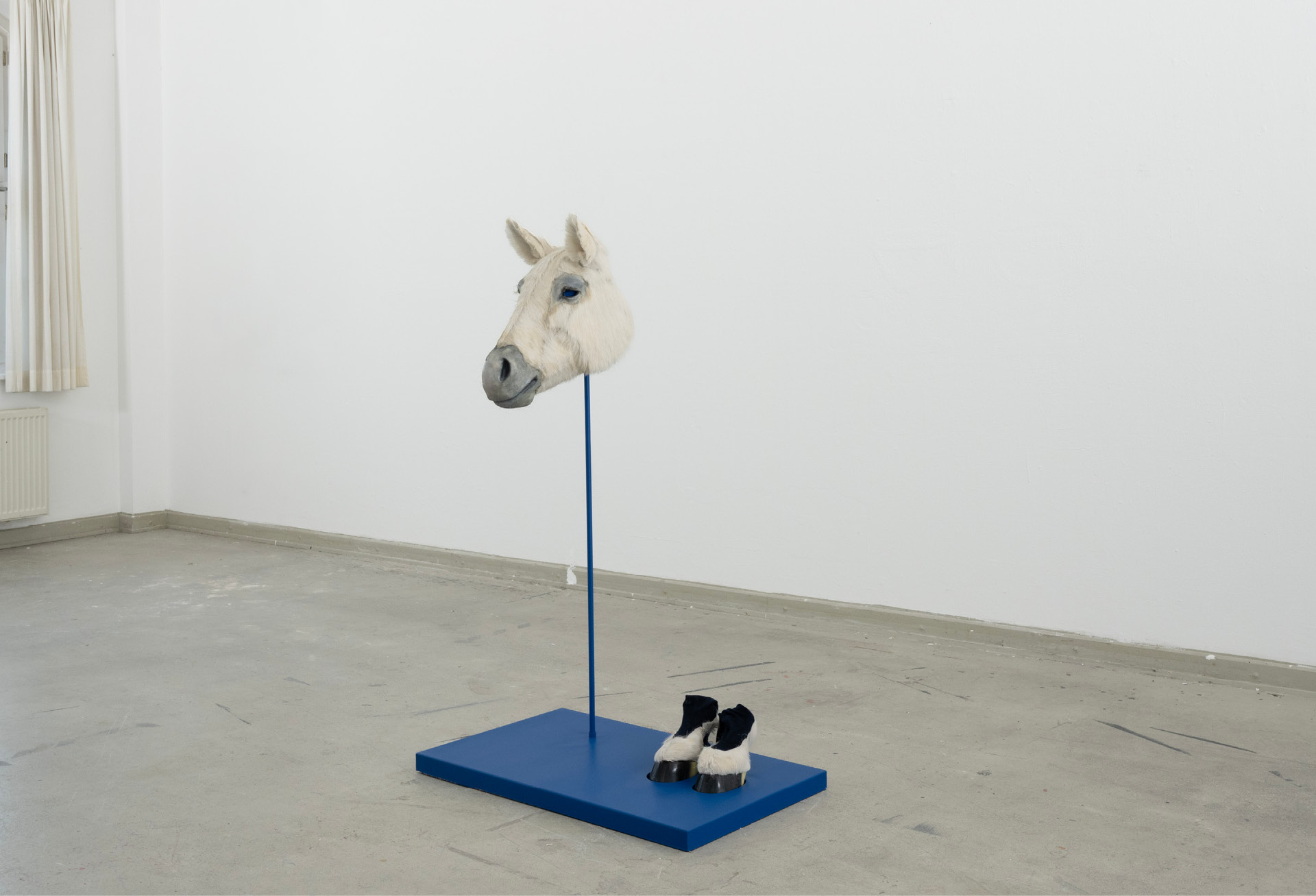Pferdefrau: a white horse head on a blue steel stem rising from a blue plinth, with hoofed shoes beside it