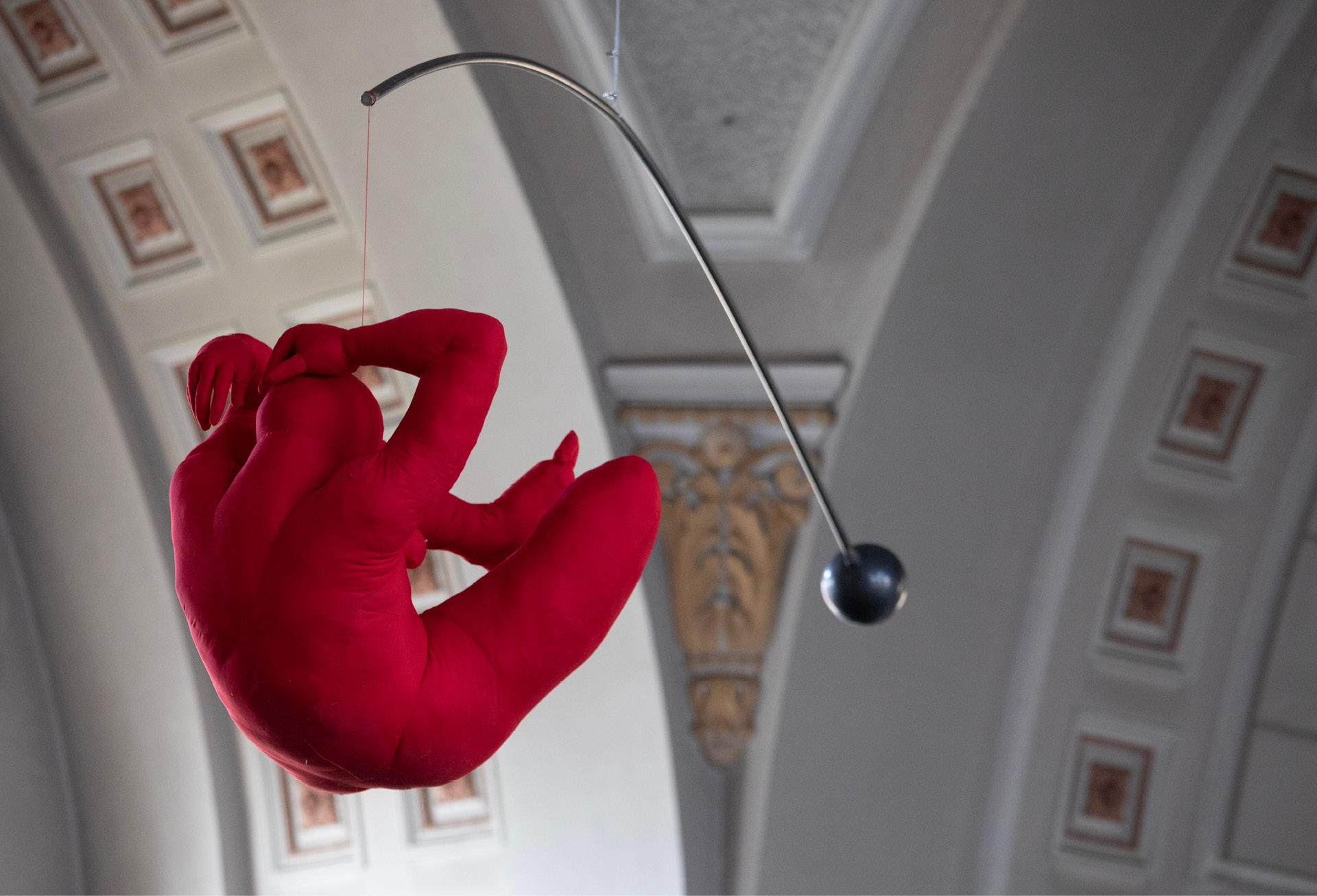 Occupation of Room: a red textile figure suspended from a steel arm in a vaulted hall